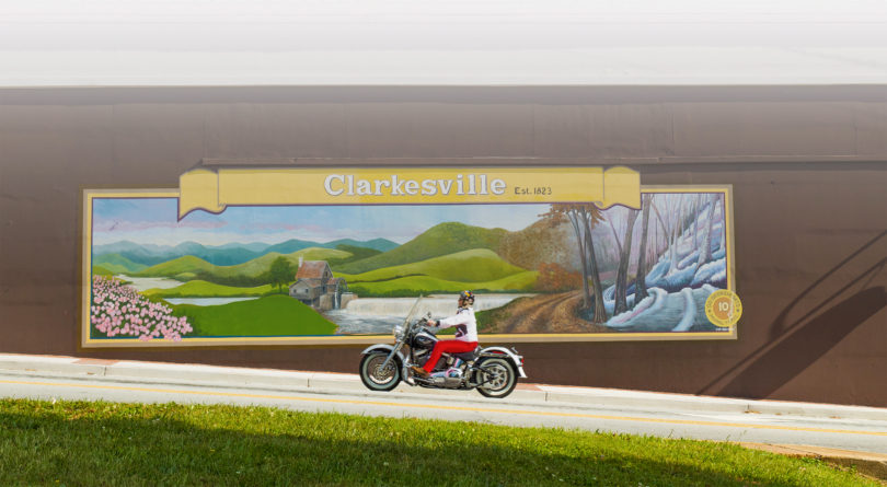 A motorcycle drives in front of a Clarkesville mural.