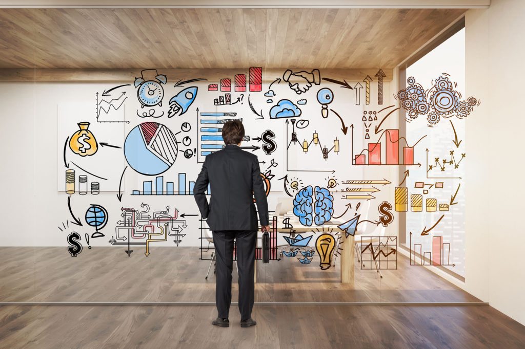 Businessman with suitcase looking at startup icons on glassboard