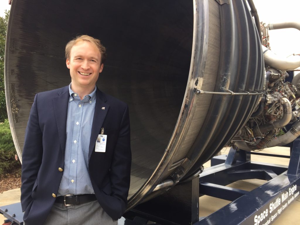 Professor Ben Davis stands in front of a Space Shuttle Main Engine. 