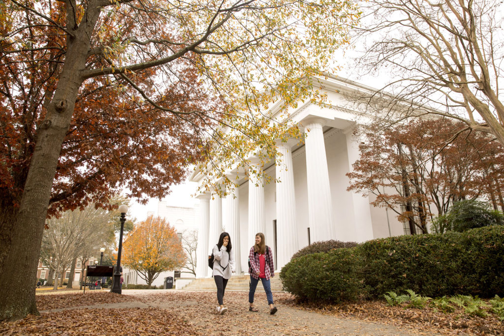 Chapel with fall leaves and students walking in front of it