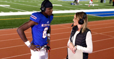 A woman interviews a football player after a football game.