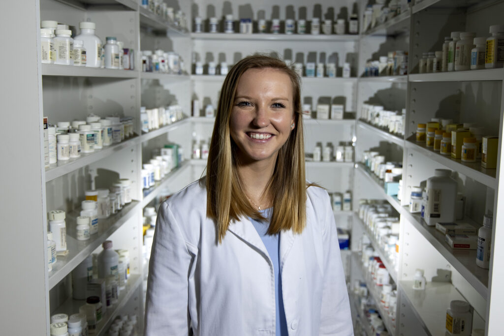 Rebecca Bruning in white pharmacist coat with pharmacy in the background
