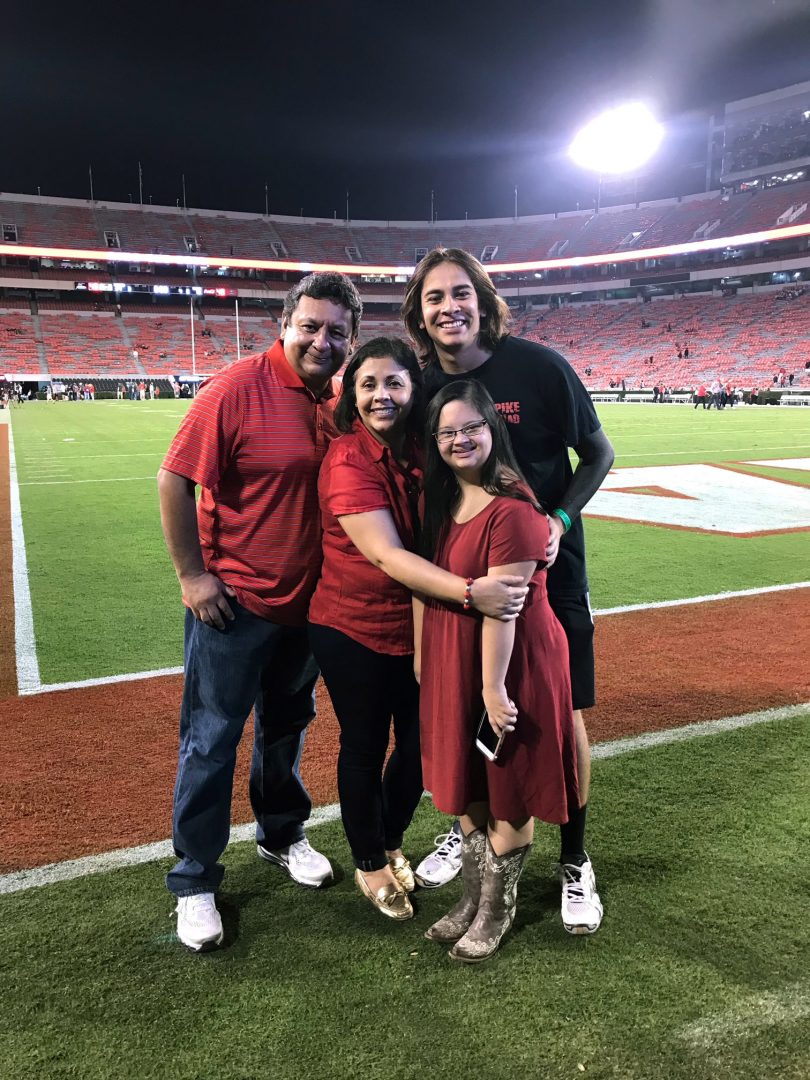 A family of four hugs with the UGA football field in the background.