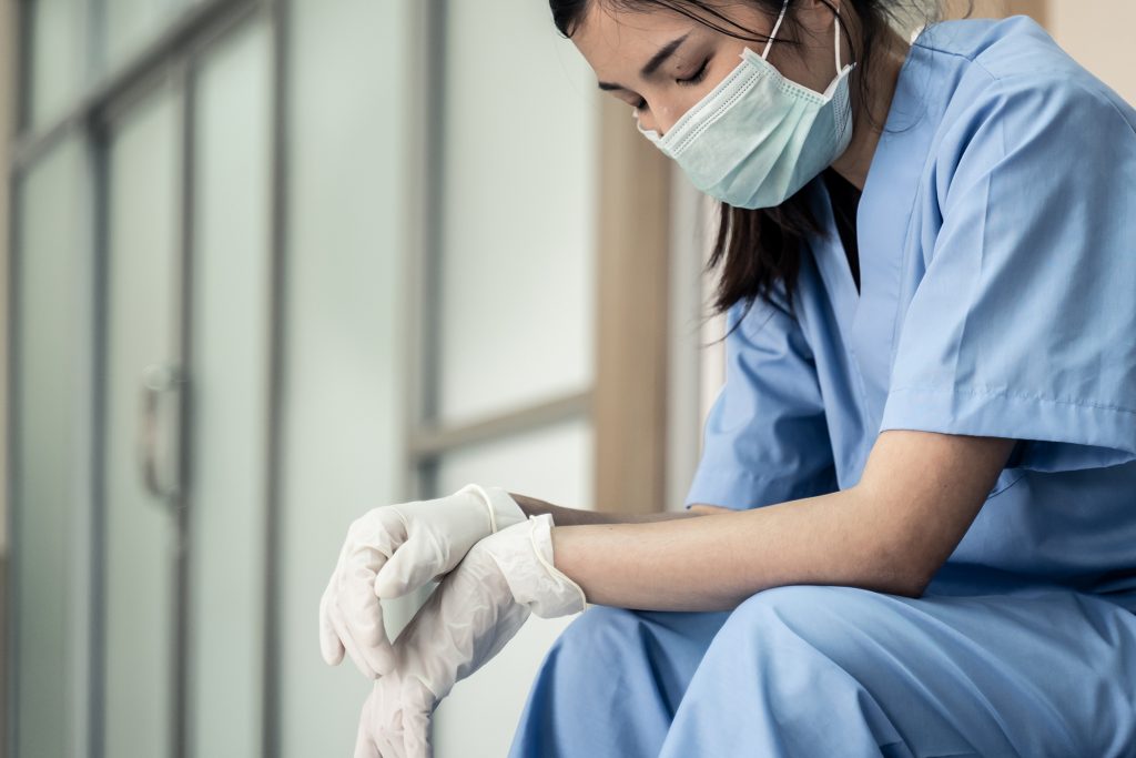 Woman in scrubs and a mask looking tired.