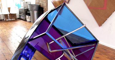 A purple and blue sculpture made of plexiglass and a chair.