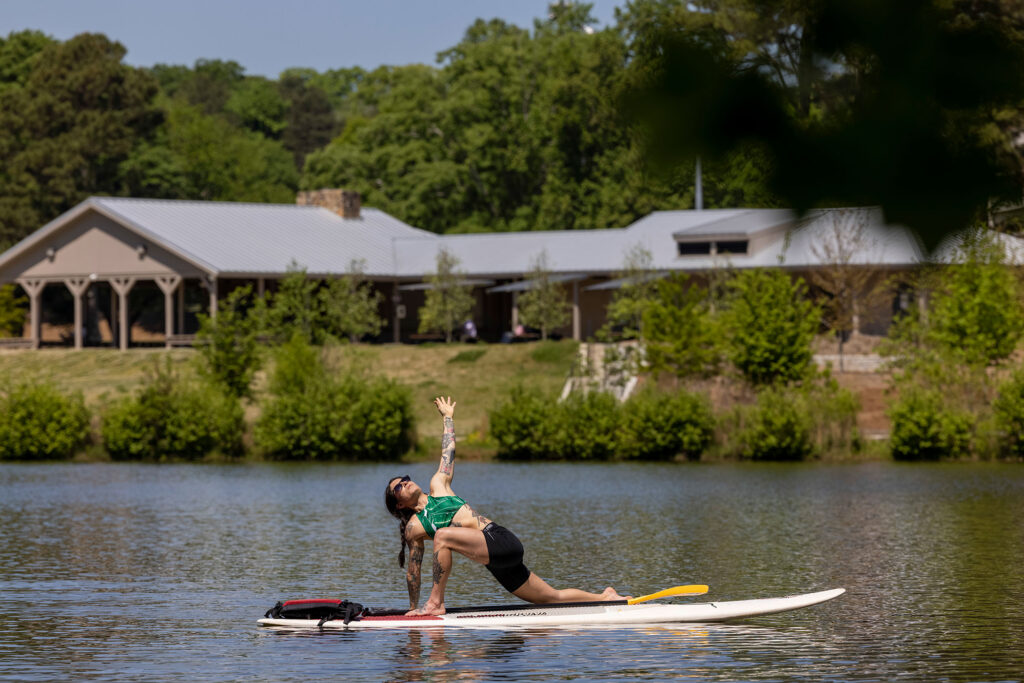 A student does a yoga pose on a paddleboard on a lake.