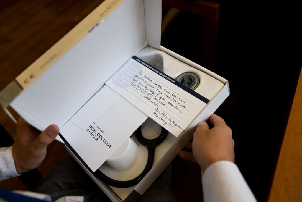 A student's hands are shown opening a box with a personal note and a new stethoscope inside it.