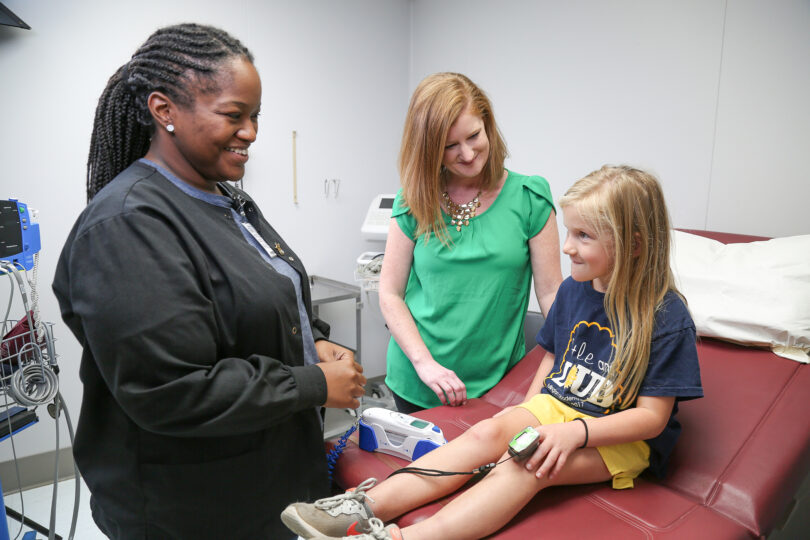 A health care worker talks with a child patient in a doctor's office.