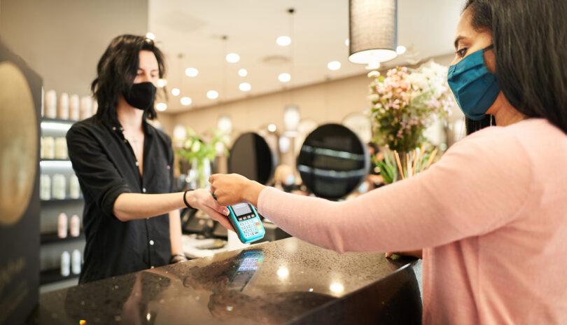 A woman at a hair salon pays contactless while wearing a protective face mask.
