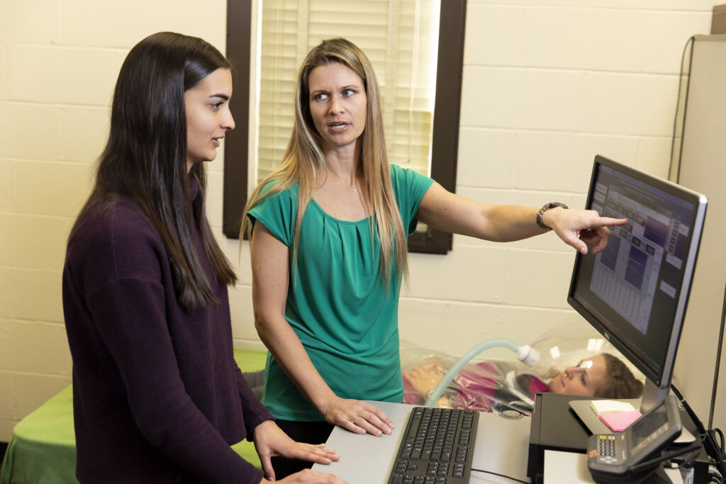 Graduate student Liana Rodrigues and professor Jamie Cooper look at a computer screen.
