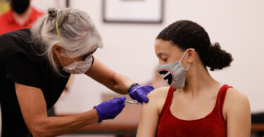 A nurse gives a vaccine shot to a student.