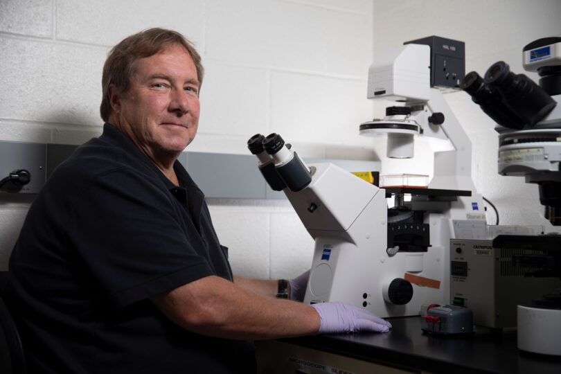 Researcher Ralph Tripp sits in front of a microscope