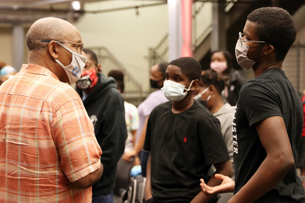 Rick Dunn wearing a face mask talks with two high school students in black shirts