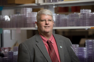 Researcher stands in lab in front of plastic trays