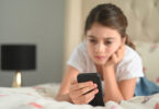 A young girl looks at her phone with a sad expression on her face.