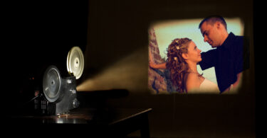 A film projector projects a scene from a movie on a screen. The image shows a couple.