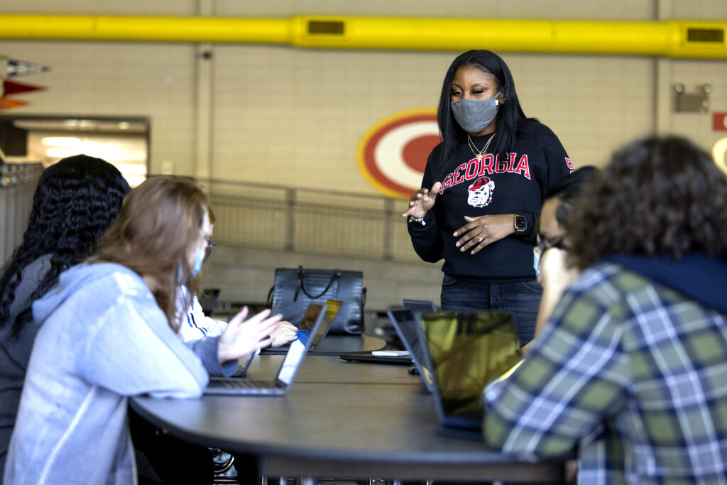 A woman wearing a mask talking to a small group of high school students