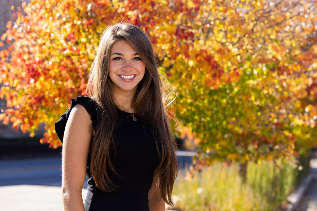 A female college student outside in front of fall foliage