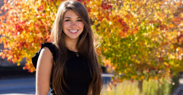 A female college student outside in front of fall foliage