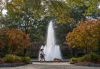 Two students walk their dog in front of the fountain at Herty Field.