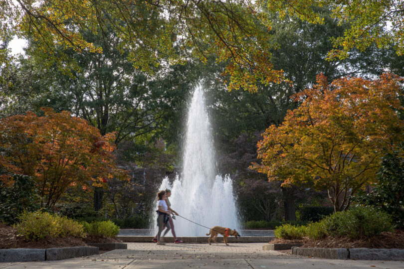 Two students walk their dog in front of the fountain at Herty Field.