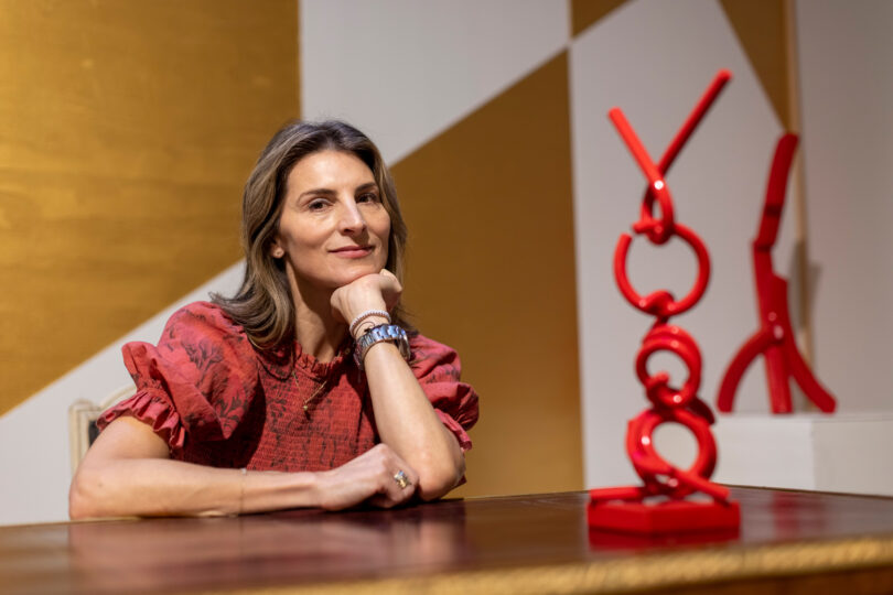 Blair Voltz Clarke is seen sitting at a table in her New York City apartment next to a red sculpture.