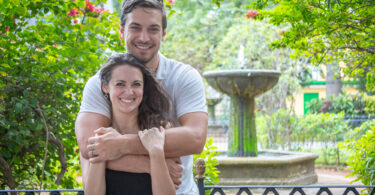 Jeremy and Lindsey pose together for a photo in a garden setting in front of a fountain.