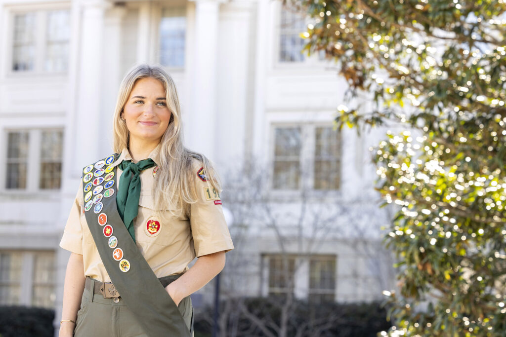 Catherine Hagerty stands in front of an academic building wearing her Eagle Scouts uniform with badges.