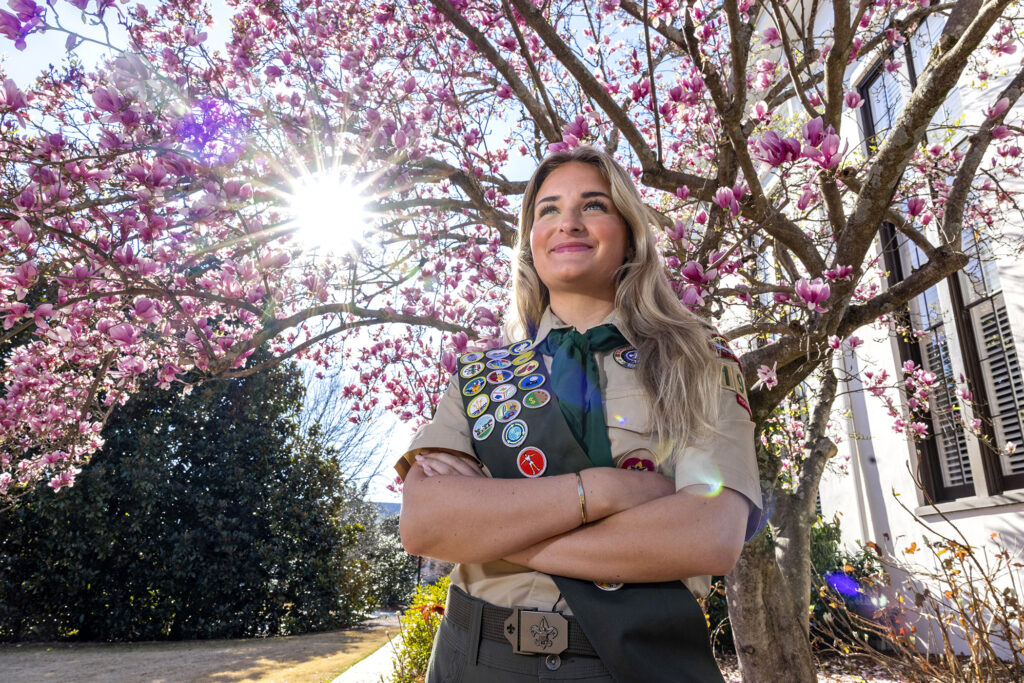 Catherine Hagerty stand in front of a blooming tree wearing her Eagle Scout uniform with badges.