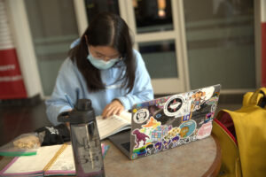 Emily Kim studies at a table in the Tate Student Center at UGA with her computer in front of her. The lid of the laptop is covered in colorful stickers. 
