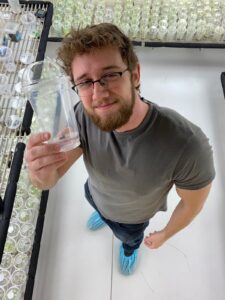 Second-year PhD student Vincent Pennetti holds a germinated seed in a plant lab.