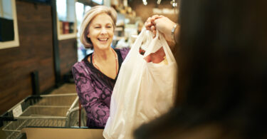 A mature woman taking a shopping bag from the cashier at a supermarket where there is no plastic bag ban.