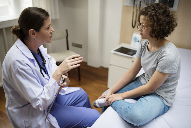 A female doctor sits down with a young female patient.