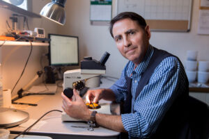Andy Davis is shown looking into the camera while holding a monarch butterfly in front of a microscope.