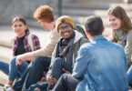 A multi ethnic group of teenagers are sitting on steps instead of exercising.