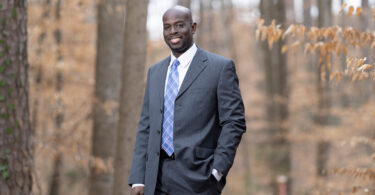 Darigg Brown is pictured standing in front of a wooded area, dressed in a suit.