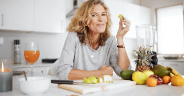 Shot of a woman preparing and eating fruit before making a smoothie