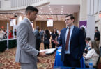A white man and an Indian student, both wearing suits, talk in the lobby of a hotel during a job fair at the University of Georgia.