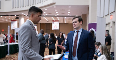A white man and an Indian student, both wearing suits, talk in the lobby of a hotel during a job fair at the University of Georgia.