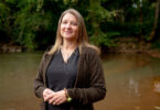 An environmental portrait of researcher Jenna Jambeck in front of greenery along a riverbank.