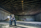 Inside a barn, a desperate looking man sitting all by himself on a bucket.