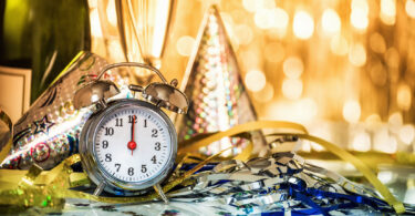 A New Year's party hat and clock are shown on a table