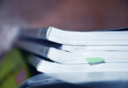 A stack of scientific journals are shown stacked on a desk with a sticky note on one of them.