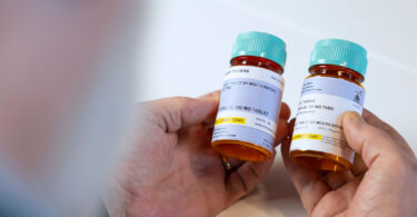 A man holds two prescription bottles in his hand, studying the difference between the traditional and new patient-friendly labels.