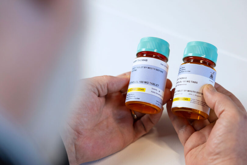 A man holds two prescription bottles in his hand, studying the difference between the traditional and new patient-friendly labels.