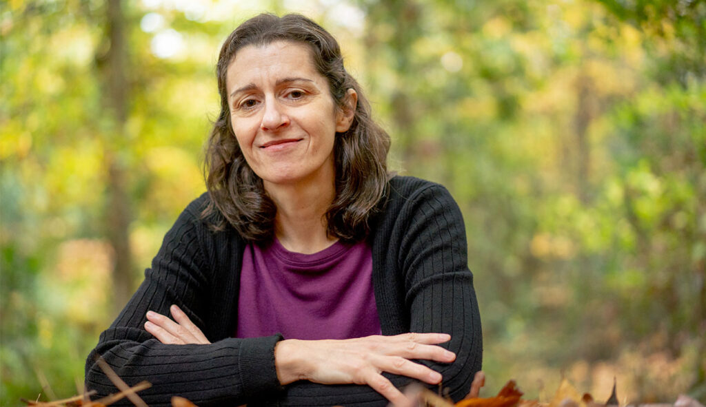 A female researcher is shown staring at the camera with her arms crossed in a forest.