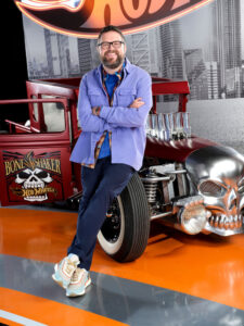 Rutledge Wood leans on an class, red automobile.