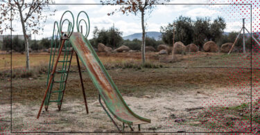 An abandoned playground with a slide is shown on an overcast day.