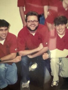 A young Rutledge Wood wearing a red polo shirt poses with other student staff of the University of Georgia Visitors Center.