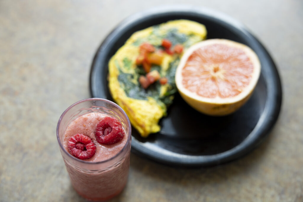An omelette with half a grapefruit and a raspberry smoothie are shown sitting on a table.